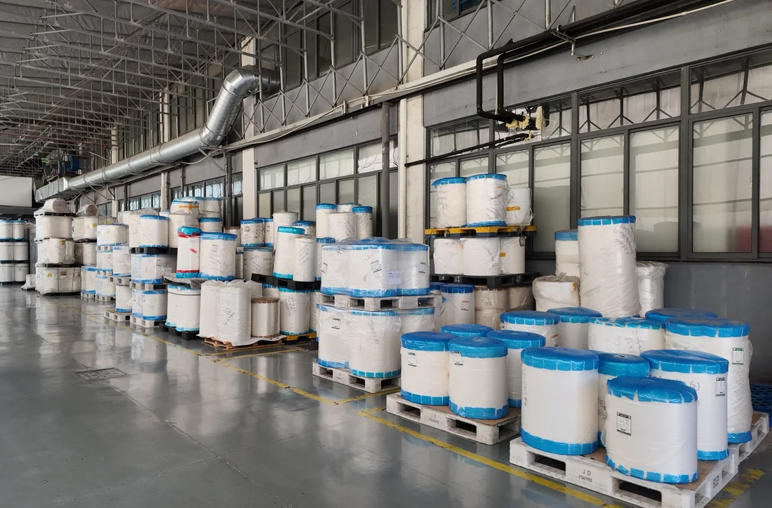 Wrapped base-film rolls stored on pallets at a partner manufacturing facility
